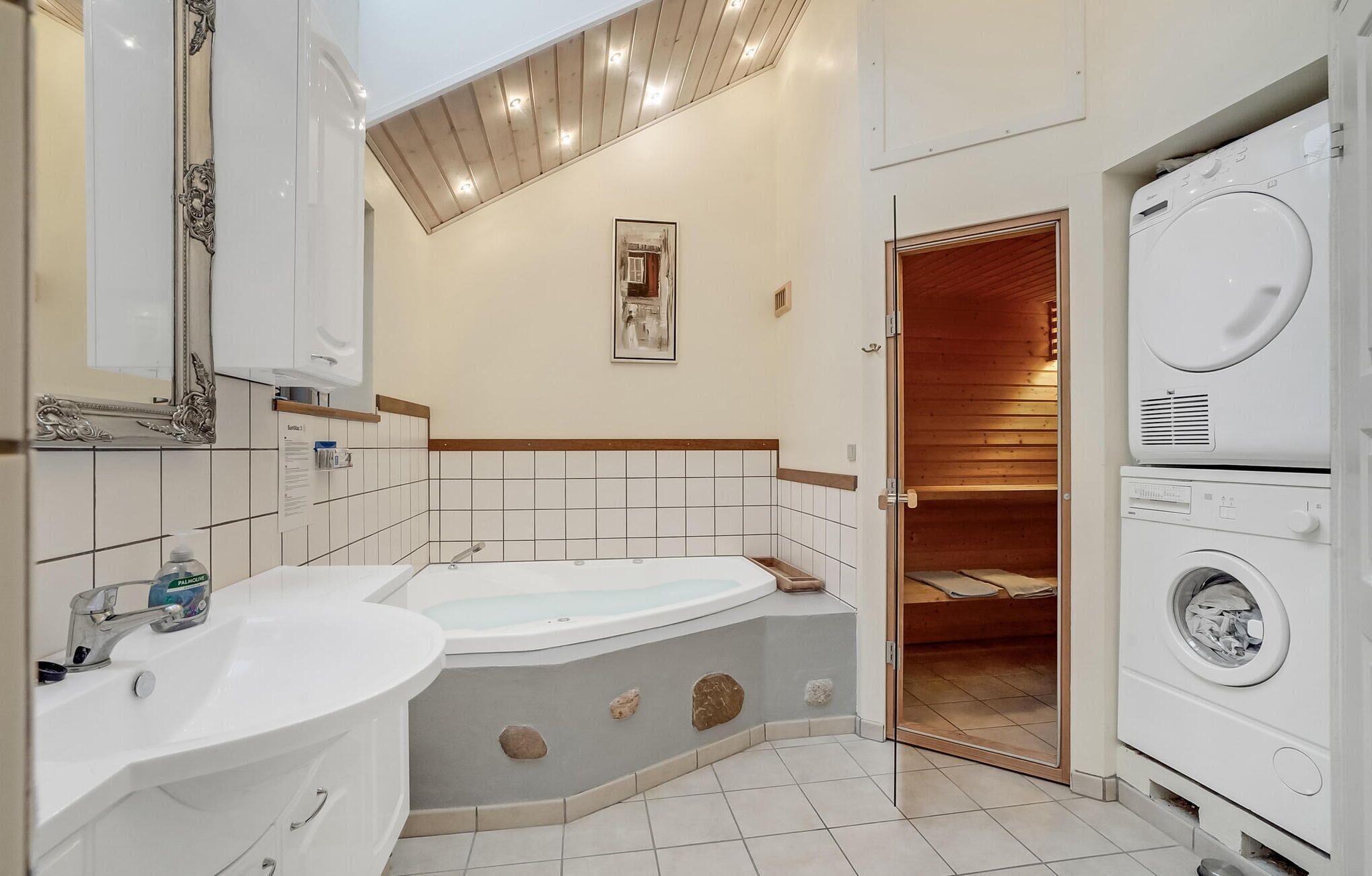 Une salle de bain avec une baignoire, un lavabo, un miroir, un tableau encadré au mur et une porte de sauna en bois.