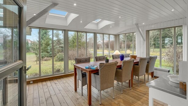 A sunroom with a wooden floor, large windows, and a table with chairs. - 3 bedroom gorgeous home in Højslev (Højslev)