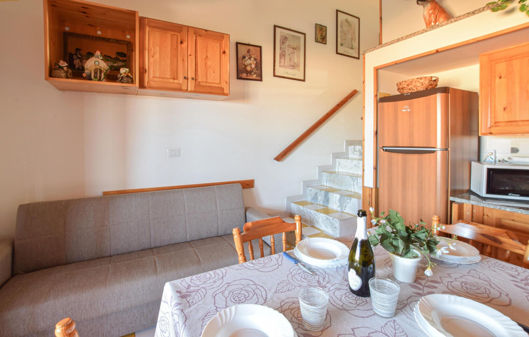 A dining area with a table set for four, a sofa, wooden cabinets, and a staircase.