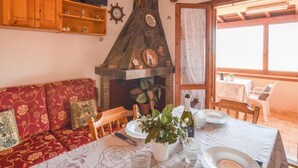 Ein gemütliches Wohnzimmer mit Kamin aus Stein, Holzmöbeln und einem Essbereich mit Tisch für zwei Personen.