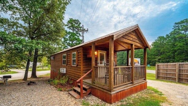 A small wooden cabin with a porch, a bench, and a gravel driveway. - Choctaw: Sleep 4, Tiny Cabin, Pets, Near Park/Lake (Broken Bow)