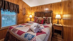 A wooden-paneled room with a bed, two bedside lamps, and a window with blinds. - Choctaw: Sleep 4, Tiny Cabin, Pets, Near Park/Lake (Broken Bow)