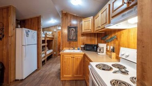 A compact kitchen with wooden cabinets, a white refrigerator, a microwave, a stove, and a sink. - Choctaw: Sleep 4, Tiny Cabin, Pets, Near Park/Lake (Broken Bow)
