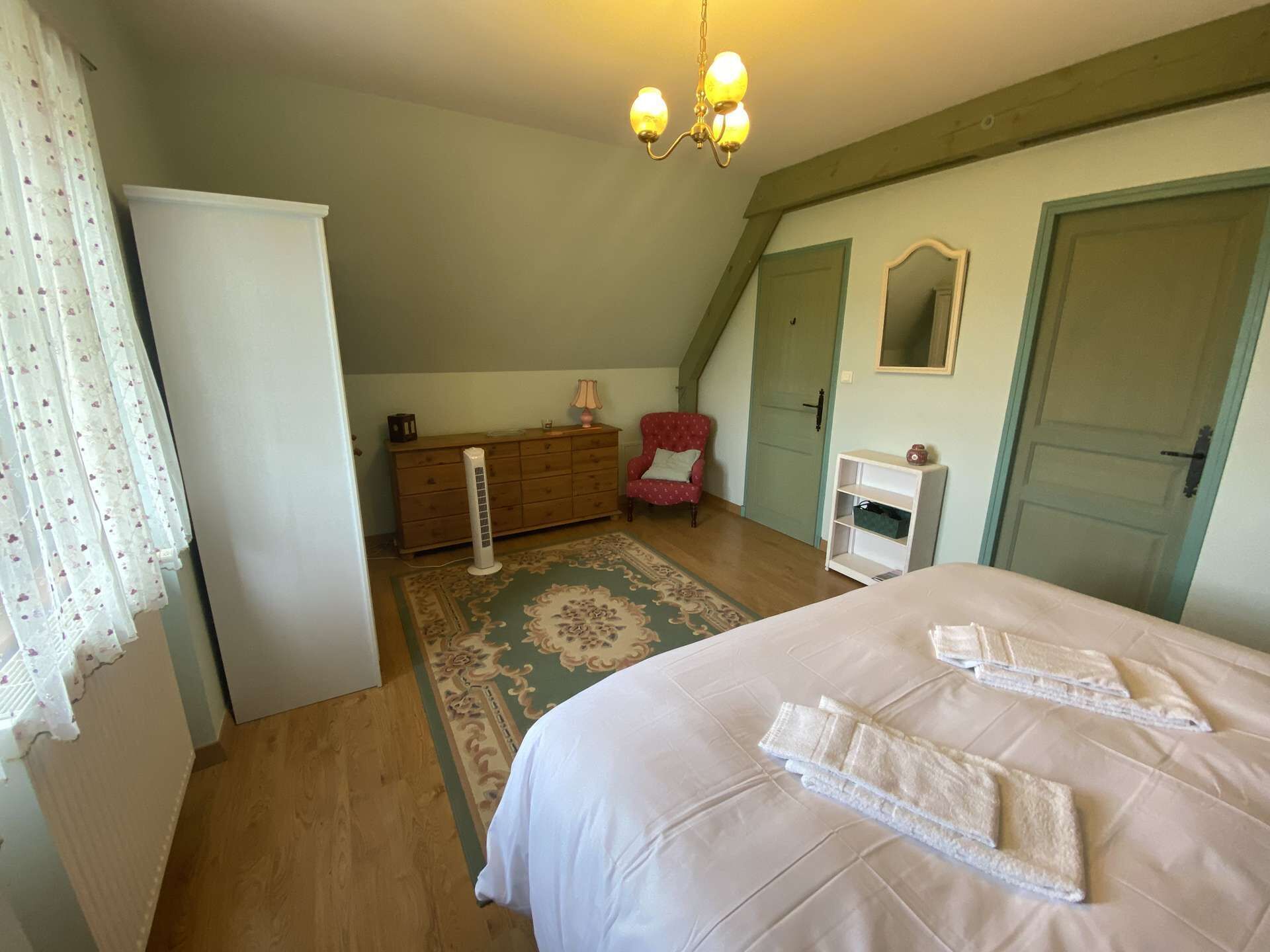 A bedroom with a large bed, a dresser, a chair, and a mirror.