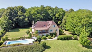Ein großes Haus mit Schwimmbecken, umgeben von üppigem Grün und Bäumen.