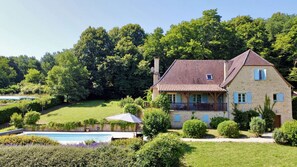 A two-story stone house with a tiled roof, surrounded by a well-maintained garden and a swimming pool.