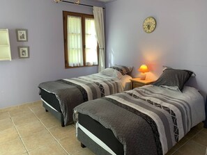 Ein Schlafzimmer mit zwei Betten, einer Nachttischlampe, einer Uhr und einem Fenster mit Vorhängen.