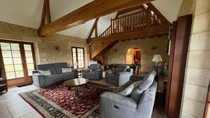 Ein geräumiges Wohnzimmer mit hoher Decke und freiliegenden Holzbalken, möbliert mit Sofas und einem Billardtisch.