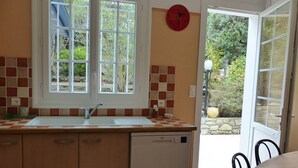 Een keuken met een raam, een spoelbak, een vaatwasser en een eethoek met stoelen.