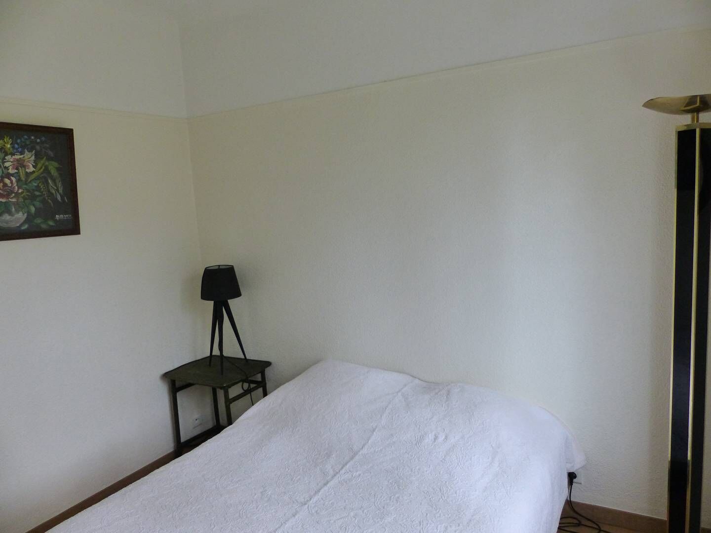 Ein Zimmer mit einem Bett, einem kleinen Tisch mit einer Lampe und einem Bild an der Wand.