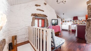 Ein rustikales Interieur mit Steinwand, Holztreppe, einer Couch, einem Fernseher und einer Küchenzeile.