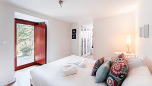 Ein Schlafzimmer mit einem großen Bett, einem Nachttisch mit Lampe, einem Fenster mit Blick auf Bäume und einer Tür, die auf einen Balkon führt.