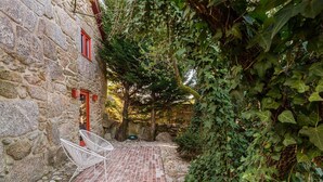 Ein Steinhaus mit roter Tür und Fenster, einer Ziegelterrasse und weißen Stühlen.