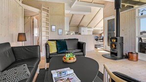 A modern living room with a black sofa, a wooden coffee table with fruit, a black fireplace, and a view of the outdoors.