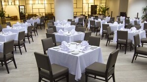 A banquet hall with multiple tables set for dining, arranged in rows with chairs.