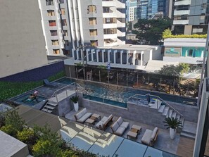 Área de piscina en la azotea con sillas de descanso y una piscina pequeña, rodeada de edificios altos.