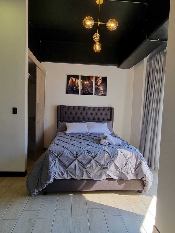 Un dormitorio moderno con cabecera capitonada, una cama grande con edredón de estampado geométrico y una araña con múltiples bombillas.