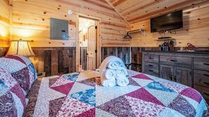 A wooden cabin interior with a bed, a television, and a kitchen area. - Willow: Sleeps 3, Tiny Cabin, Pets, Near Lake/Park (Broken Bow)