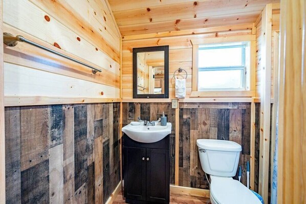 Une salle de bain rustique, aménagée dans une cabane en bois, avec un lavabo, un miroir et des toilettes.