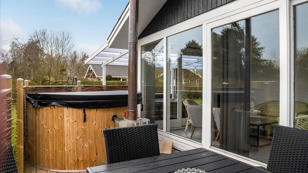 Eine Terrassenanlage mit Whirlpool, Sitzgelegenheiten im Freien und einer großen Schiebeglastür, die zu einem überdachten Außenbereich führt.