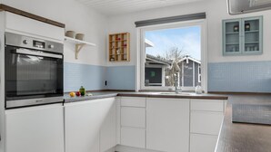 Eine moderne Küche mit weißen Schränken, einem eingebauten Ofen und einem Fenster mit Blick auf ein Haus.