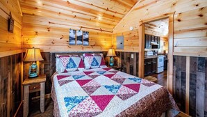 Interior de uma cabana de madeira com cama, cozinha e banheiro.