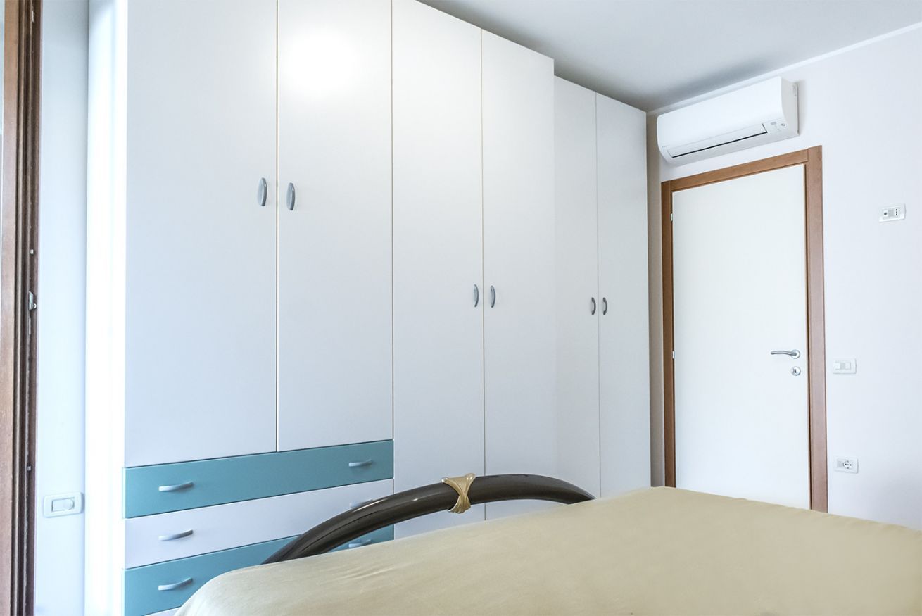 Une chambre à coucher comprenant un lit, une armoire avec de nombreux tiroirs et une porte équipée d’un appareil de climatisation.