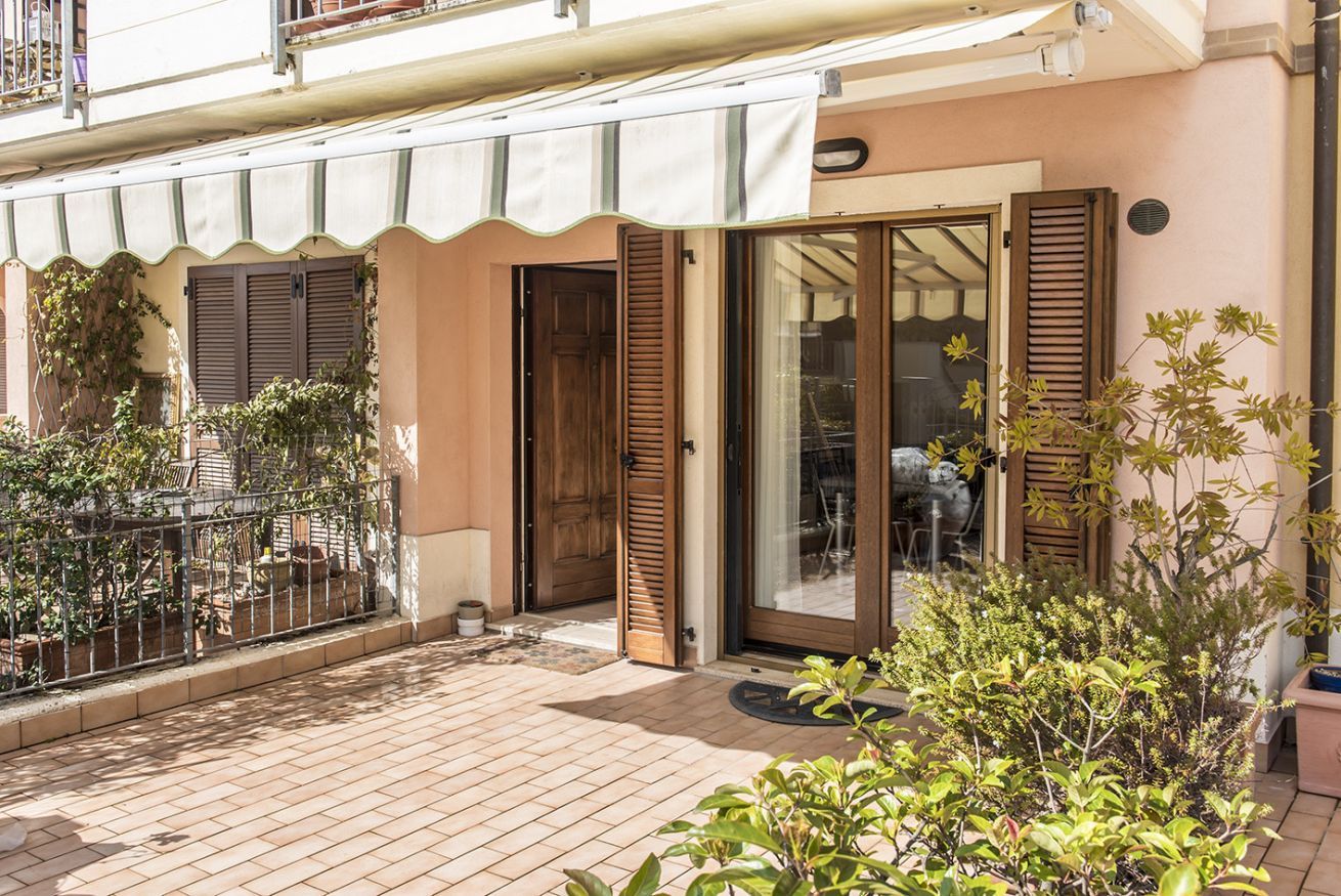 Un immeuble résidentiel doté d’un patio carrelé, de volets en bois et d’une entrée abritée.