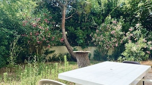 Une terrasse avec une table et des chaises blanches, entourée d’une végétation luxuriante et de plantes en fleurs.