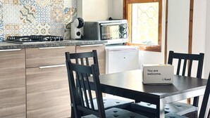 Une cuisine équipée d’une cuisinière à gaz, d’un grille-pain et d’un réfrigérateur. On y trouve une table avec une chaise et une boîte de bienvenue.