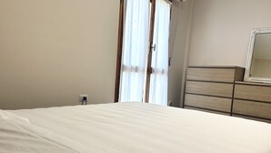 Une chambre à coucher avec un lit, une commode, un miroir et une fenêtre avec des rideaux.