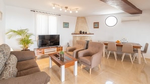Una sala de estar moderna con sofá, sillón, televisor, chimenea, mesa de comedor y sillas.