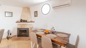 Un coin repas agrémenté d’une cheminée en pierre, d’une table ronde avec des sets de table et d’un chandelier orné de bougies.
