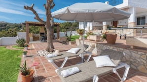 Un patio con sillones de descanso, un árbol y una sombrilla grande.