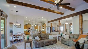 A spacious living room with a large sofa, a coffee table, and a dining area with wooden furniture. There is a kitchen in the background with wooden cabinets and a ceiling fan. - Custom home with heated spa and pool, 1 acre, No HOA, bring Rvs (Phoenix)