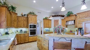 A kitchen with wooden cabinets, a central island with chairs, and various appliances. - Custom home with heated spa and pool, 1 acre, No HOA, bring Rvs (Phoenix)