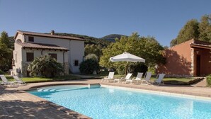A swimming pool with lounge chairs and umbrellas, surrounded by a house and greenery. - Residenze di Campagna (Alghero)
