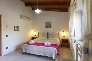 Ein Schlafzimmer mit Bett, Nachttischen, einer Pendelleuchte, einem Bild an der Wand und einem Fenster mit Vorhängen.