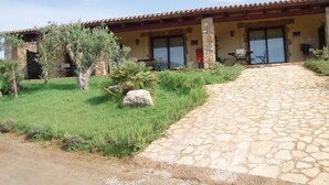 A building with a stone pathway leading to a covered patio area with outdoor seating. - Residenze di Campagna (Alghero)