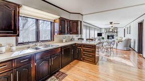 A spacious kitchen with dark wooden cabinets, a large island, and a view of the living area. - Peaceful Niangua River Retreat (Buffalo)
