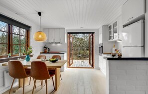 A modern kitchen with white cabinetry, a dining area with wooden furniture, and a large window overlooking a garden. - 3 bedroom beautiful home in Ringkøbing (Ringkøbing)
