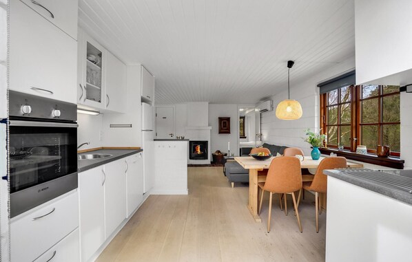 A modern kitchen with white cabinetry, a Bosch oven, and a dining area with a wooden table and orange chairs. - 3 bedroom beautiful home in Ringkøbing (Ringkøbing)