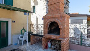 Un horno de ladrillo al aire libre, una silla de plástico blanco y una puerta verde.