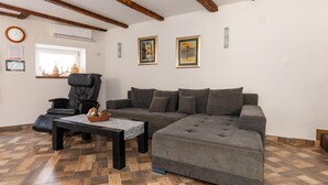 Una sala de estar con un sofá modular, un sillón de cuero, una mesa de centro de madera y un tapete estampado. Hay dos cuadros enmarcados en la pared y un reloj.