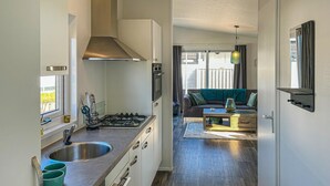 A compact kitchen with a gas stove, stainless steel sink, and modern cabinetry. A dining area with a wooden table and a sofa is visible through an open doorway. - Awesome home in Scherpenisse with WiFi (Scherpenisse)