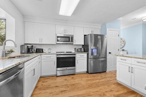 Une cuisine moderne avec des armoires blanches, des appareils en acier inoxydable et un plancher en bois.