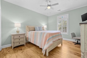 A bedroom with a bed, nightstand, lamp, chair, and a ceiling fan.