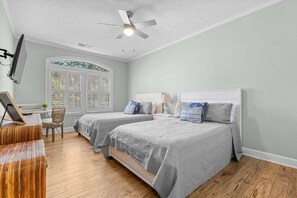 Une chambre avec deux lits, un ventilateur de plafond, une fenêtre avec vue et un bureau avec une chaise.