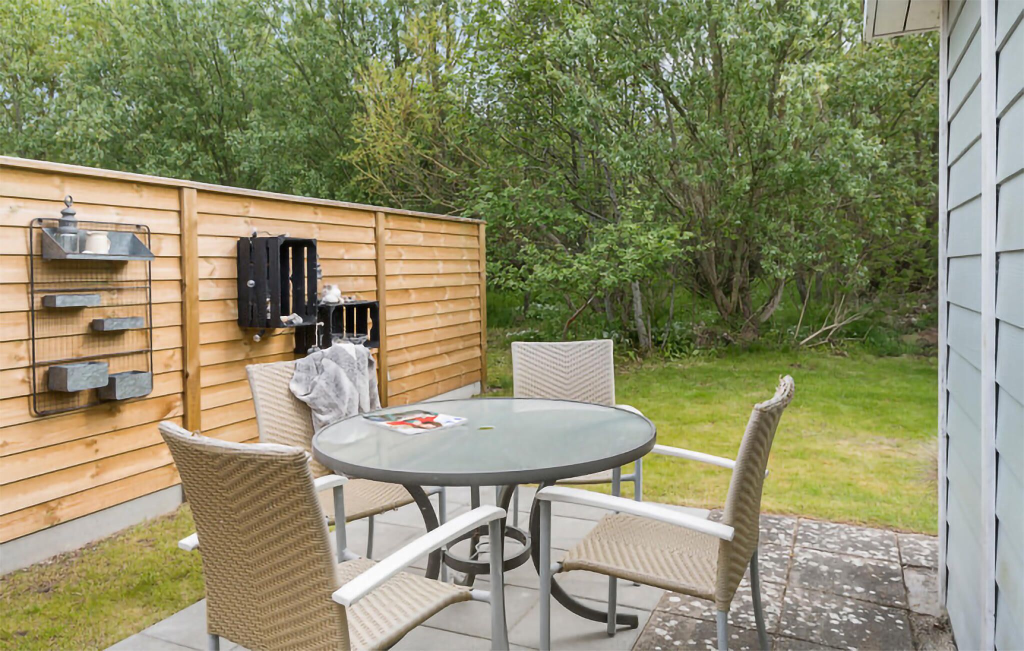 A patio with a round table and four chairs, a wooden fence, and a grill.