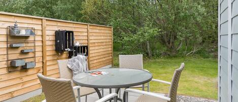 A patio with a round table and four chairs, a wooden fence, and a grill.